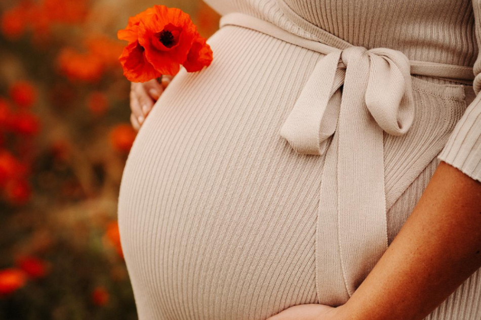 Soins mamans : femme métisse enceinte tenant une fleur de coquelicot