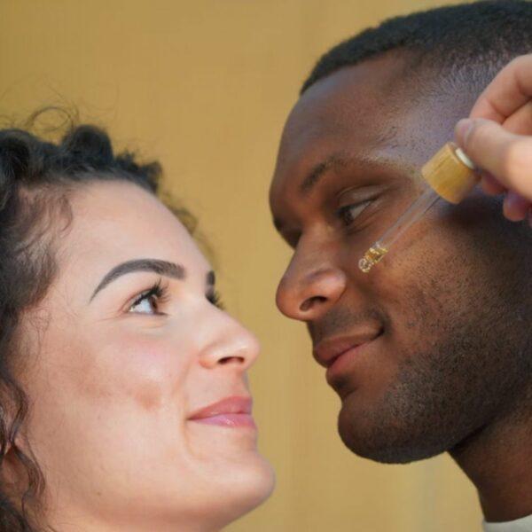 Sérum visage Skin City MIRA - jeune femme blanche versant une goutte de sérum sur la joue d'un jeune homme noir